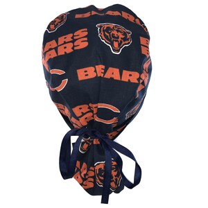 May include: A navy blue surgical scrub hat with a tie, featuring a repeated pattern of orange Chicago Bears logos and the word "Bears".
