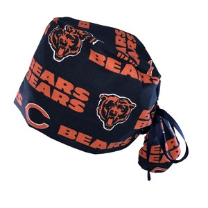 May include: A navy blue surgical scrub hat with a tie. The hat is covered in a repeating pattern of orange bears and the word "Bears".