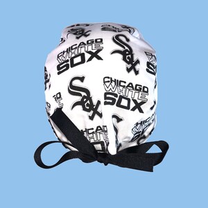 May include: White surgical scrub hat with a black and white print of the Chicago White Sox logo. The hat has a black tie.