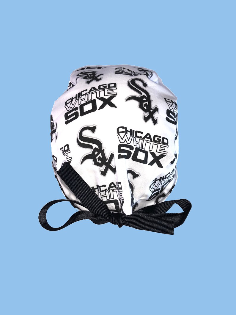 May include: White surgical scrub hat with a black and white print of the Chicago White Sox logo. The hat has a black tie.