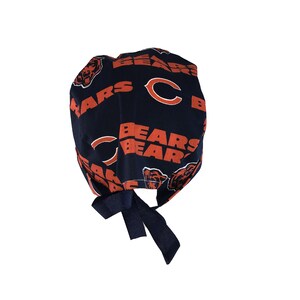 May include: A navy blue surgical scrub hat with a repeating pattern of orange Chicago Bears logos and the letter "C". The hat has a black tie.