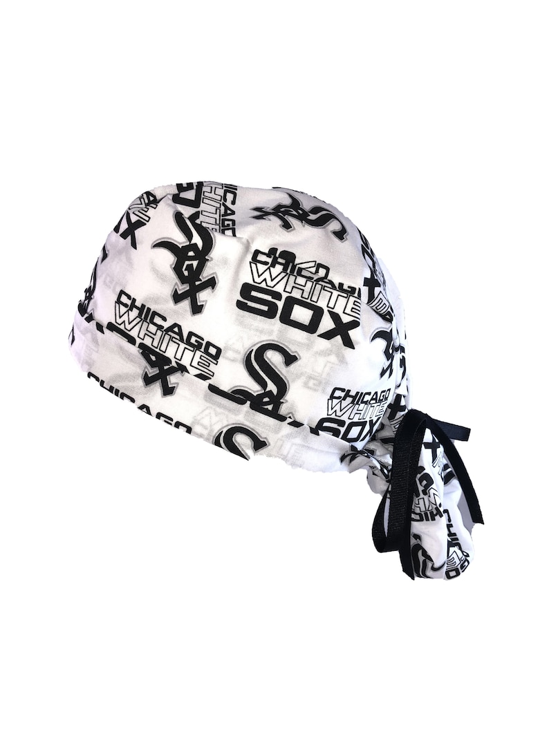 May include: White surgical scrub hat with a black and white print of the Chicago White Sox logo and team name. The hat has a black tie.