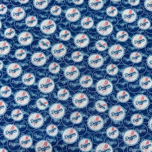 May include: Blue fabric featuring a repeating pattern of the Los Angeles Dodgers logo. The logo is in a white circle with red accents and the word "Dodgers" in script. The background is a dark blue with a lighter blue circular design.