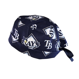 May include: A navy blue surgical scrub hat with a repeating pattern of the Tampa Bay Rays logo. The hat has a tie on the back.