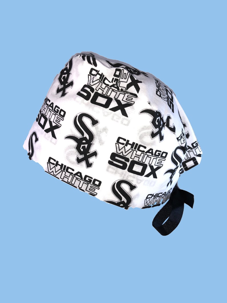 May include: White and black patterned surgical scrub hat with a black tie. The pattern features the Chicago White Sox logo and text.
