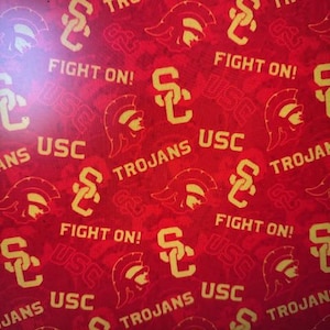 May include: Red fabric with a repeating pattern of yellow USC logos, Trojan helmets, and the words "TROJANS" and "FIGHT ON!". The design is a bold, eye-catching pattern.