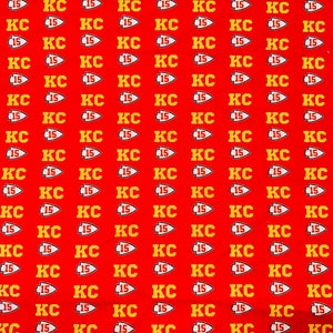 May include: Red fabric with a repeating pattern of yellow "KC 15" logos. The logos are in a stylised font with a small arrow pointing to the right.