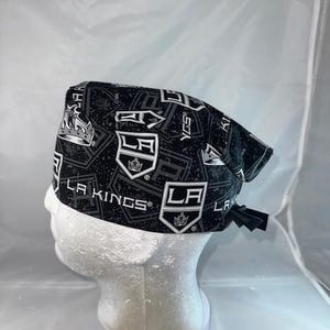 May include: Black and white patterned surgical scrub hat with the LA Kings logo repeated throughout. The hat has a tie on the back.