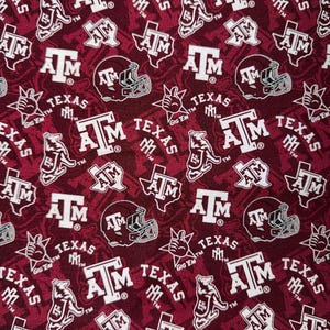 May include: A maroon fabric featuring a repeating white pattern of Texas A&M University logos, including the ATM monogram, the state of Texas outline, a football helmet, a mascot, and a hand gesture with the text Gig 'Em and Texas.