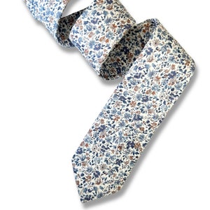 May include: A white tie with a blue and brown floral pattern. The tie is made of a soft, comfortable fabric and is perfect for adding a touch of style to any outfit.