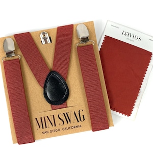 May include: Cinnamon-colored suspenders with silver-tone clips and a black leather connector. The suspenders are displayed on a brown card with the text "MINI SWAG SAN DIEGO, CALIFORNIA". A fabric swatch labeled "Cinnamon" by David's Bridal is also included.