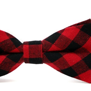 May include: A red and black buffalo plaid bow tie. The bow tie is made of fabric and features a classic checkered pattern. The bow tie is a formal accessory.