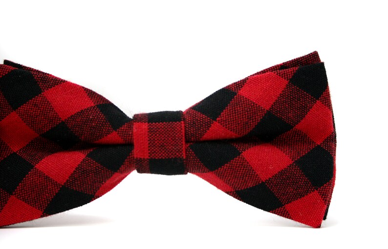 May include: A red and black buffalo plaid bow tie. The bow tie is made of fabric and features a classic checkered pattern. The bow tie is a formal accessory.