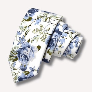 May include: A folded necktie with a white background and a floral pattern. The pattern features blue and light blue roses, green leaves, and delicate sprigs. The tie is made of a soft fabric.