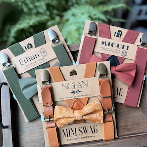 May include: Three sets of suspenders and bow ties in green, orange, and red. Each set includes suspenders, a bow tie, and a card with a name and text. The text includes "Ethan", "Miguel", and "Nolan". The bow ties have different patterns.