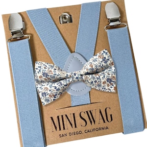Könnte beinhalten: Ein hellblaues Hosenträger- und Fliegen-Set. Die Fliege hat ein Blumenmuster mit braunen, weißen und blauen Blumen. Das Set ist auf einer braunen Karte mit dem Text "MINI SWAG SAN DIEGO, CALIFORNIA" verpackt.