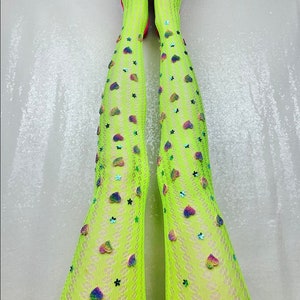 May include: Bright neon green fishnet stockings adorned with colorful heart and star embellishments. The stockings are paired with pointed-toe, hot pink heels featuring silver buckle details. A fun and fashionable accessory.
