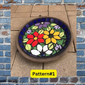 Peut inclure: Un bain d'oiseaux rond en céramique brune avec une mosaïque de fleurs. La mosaïque présente des fleurs rouges, jaunes, blanches, violettes et vertes sur un fond bleu. Le texte "Pattern#1" est imprimé sur un rectangle jaune sous le bain d'oiseaux.