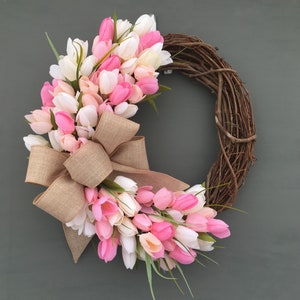May include: A pink and white tulip wreath with a burlap bow. The wreath is made of grapevine and is decorated with pink and white tulips.