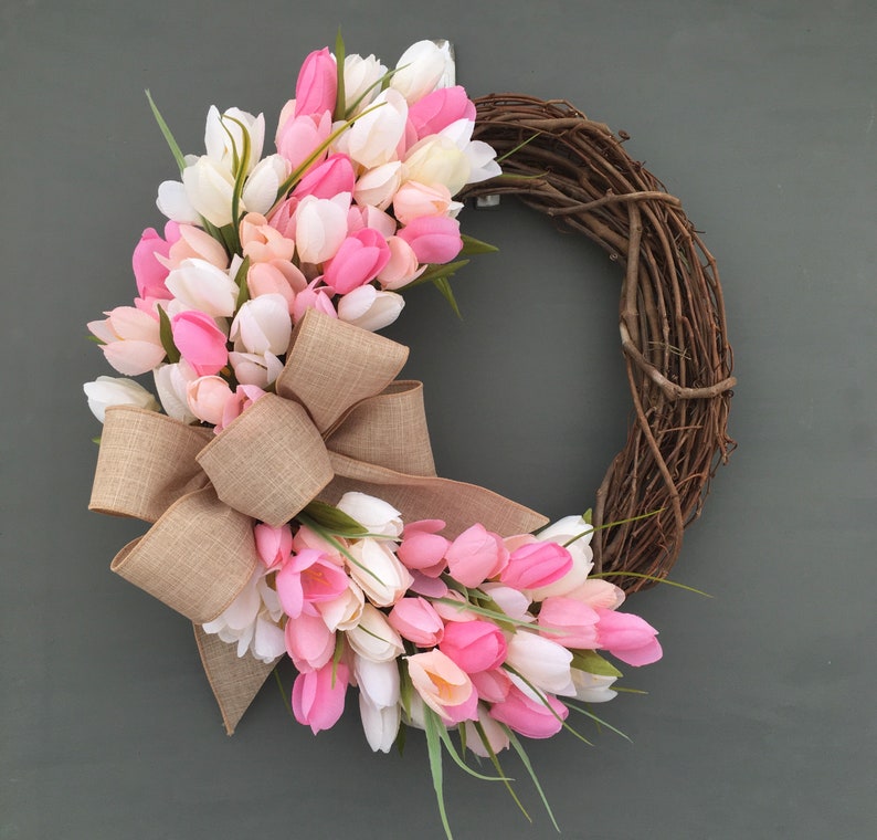 May include: A pink and white tulip wreath with a burlap bow. The wreath is made of grapevine and is decorated with pink and white tulips.
