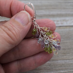May include: Silver dangle earrings with a cluster of light green, yellow, and purple gemstones.