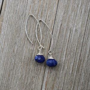 May include: A pair of silver dangle earrings with blue gemstone drops. The earrings have a simple, elegant design.