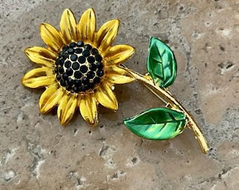May include: A gold-tone sunflower brooch with black rhinestone accents and green enamel leaves.