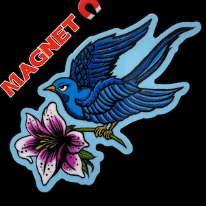 May include: A blue bird with detailed feathering perches on a stem holding a pink and white flower. The bird is set against a light blue background, with the word "MAGNET" and a magnet graphic in the upper left corner. The background is black.