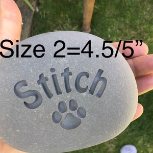 May include: A gray stone with the name "Stitch" engraved on it, along with a paw print. The stone is approximately 4.5 inches in diameter. The text "Size 2=4.5/5" is visible in the image.