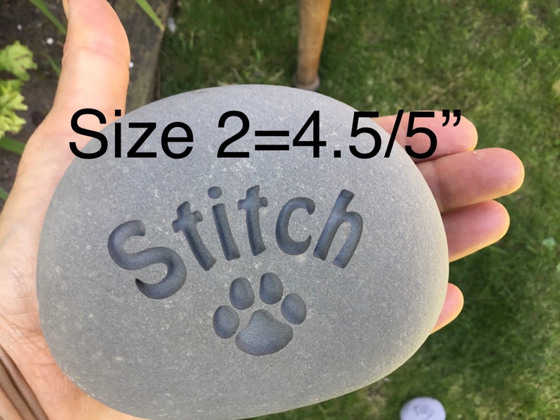 May include: A gray stone with the name "Stitch" engraved on it, along with a paw print. The stone is approximately 4.5 inches in diameter. The text "Size 2=4.5/5" is visible in the image.