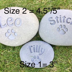 May include: Three gray, oval-shaped stones with engraved names and paw prints. The stones are labeled "Size 1 = 3" inches, "Size 2 = 4.5"/5" inches. The names on the stones are "Leo", "Stitch", and "Tilly".