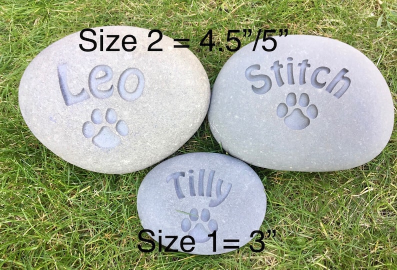May include: Three gray, oval-shaped stones with engraved names and paw prints. The stones are labeled "Size 1 = 3" inches, "Size 2 = 4.5"/5" inches. The names on the stones are "Leo", "Stitch", and "Tilly".