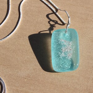 May include: A silver chain necklace with a light blue glass pendant. The pendant has a speckled, cloudy appearance.