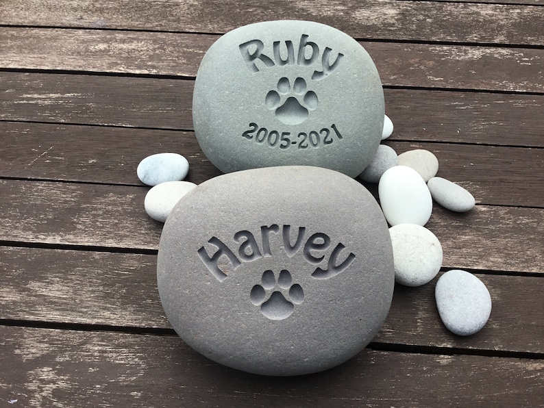 May include: Two gray stones with engraved paw prints and names. The top stone reads "Ruby 2005-2021". The bottom stone reads "Harvey".