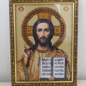Pu&ograve; includere: Un'icona religiosa incorniciata con un'immagine di Ges&ugrave; in perline, che tiene un libro aperto. Il libro contiene testo in scrittura cirillica. La cornice &egrave; dorata con dettagli decorativi.