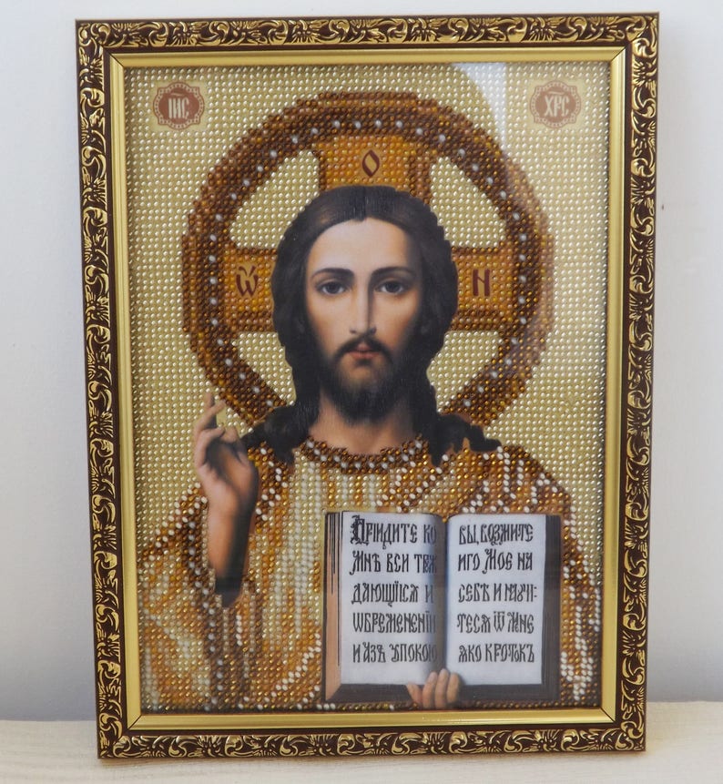 Pu&ograve; includere: Un'icona religiosa incorniciata con un'immagine di Ges&ugrave; in perline, che tiene un libro aperto. Il libro contiene testo in scrittura cirillica. La cornice &egrave; dorata con dettagli decorativi.