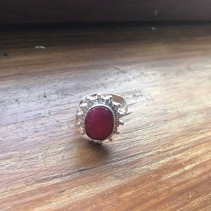 Può includere: Un anello d'argento con una pietra ovale di colore rosso scuro incastonata in un design testurizzato a forma di sole.
