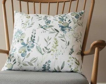 May include: A square cushion with a botanical print featuring blue, green, and white floral and foliage designs. The cushion is placed on a grey upholstered chair, creating a cosy and inviting aesthetic.