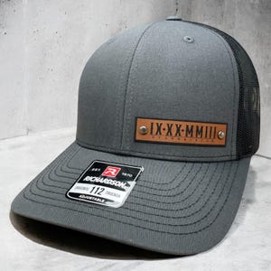 May include: Gray and black trucker hat with a brown leather patch that says "IX-XX-MMIII RYANNA & JACOB"