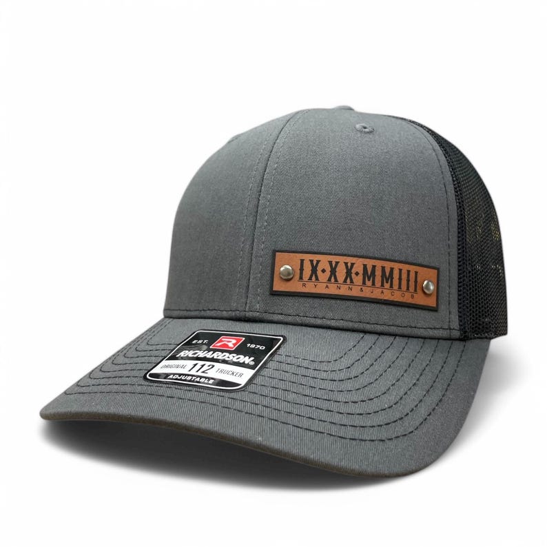 May include: A grey and black trucker hat with a brown leather patch that says "IX-XX-MMIII RYANNAJADE".