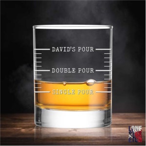 May include: A clear glass rocks glass with etched markings for a single, double, and "David's" pour of whiskey. The glass is filled with amber-colored whiskey.