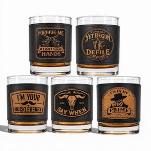 May include: Five whiskey glasses with black leather wraps. Each wrap has a different design and text, including "Forgive Me," "I Have Not Yet Begun," "I'm Your Huckleberry," "Say When," and "I'm in My Prime."