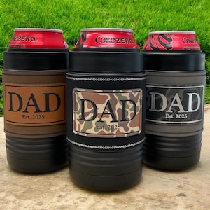 May include: Three black insulated drink holders with "DAD Est. 2025" on them. One has a brown leather-like patch, one has a camouflage patch, and one has a gray camouflage patch. Each holder has a red Coke Zero can inside.