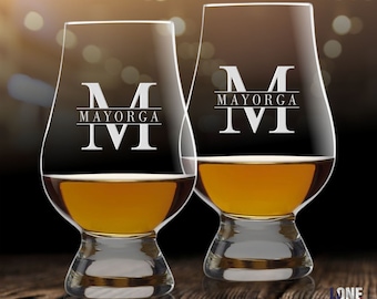 May include: Two clear glass whiskey glasses with a personalized engraved design. The glasses are filled with amber liquid and have a rounded base. The engraving reads "MAYORGA M".
