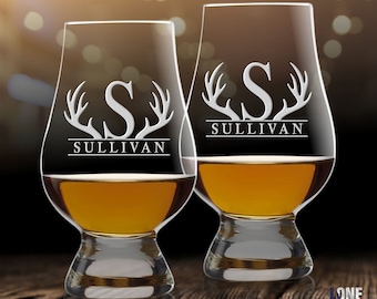 May include: Two clear glass whiskey glasses with a personalized design. Each glass features a white etched letter "S" with antlers on either side and the name "Sullivan" below. The glasses are filled with amber liquid.