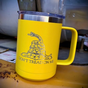 May include: A yellow stainless steel travel mug with a black and white image of a coiled snake with the words "Don't Tread On Me".