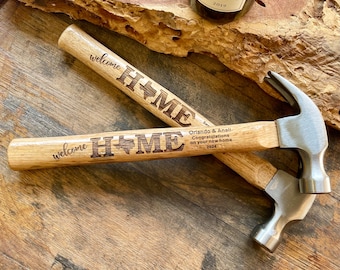 May include: Two wooden hammers with the words "Welcome Home" engraved on them. The hammers are on a wooden surface. One hammer has a Texas-shaped star and the other has a heart-shaped star.