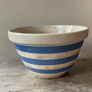 May include: A large ceramic mixing bowl featuring a wide rim and a rounded base. The exterior is decorated with alternating horizontal bands of solid blue and a distressed, off-white cream colour, creating a classic striped pattern throughout.
