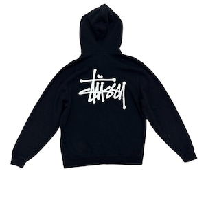 May include: Black hooded sweatshirt with a white logo on the back. The sweatshirt has long sleeves and a hood. The logo is a stylized signature. The garment is made of a soft material.