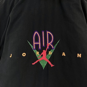Pu&ograve; includere: Camicia nera con bottoni e un logo ricamato verde, viola e arancione che dice "AIR JORDAN" con una silhouette di un giocatore di basket.